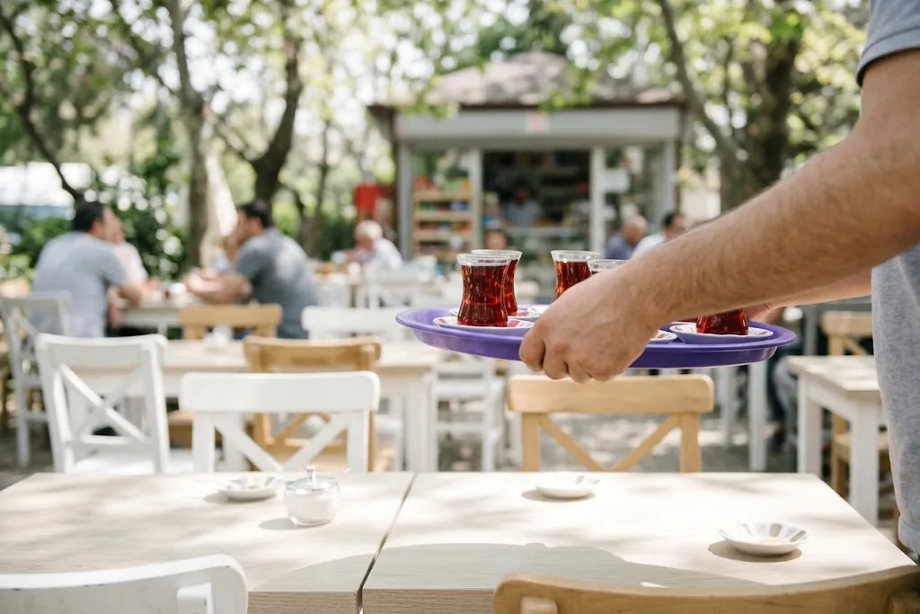 Çay bahçesinde masalar arasında taşınan mor tepside çay bardakları; binadan ve modemden uzakta